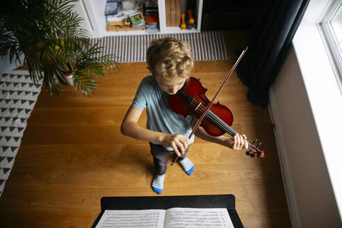 Junge mit blondem Haar übt zu Hause vor einem Notenblatt Geige - NJAF00688