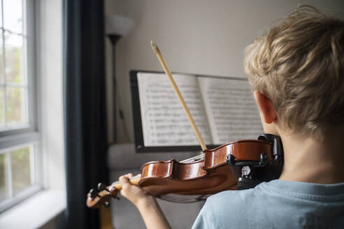 Boy practicing violin with sheet music at home - NJAF00690