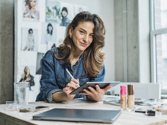 Lächelnder Influencer mit Tablet-PC am Schreibtisch in der Wohnung - MFF09486