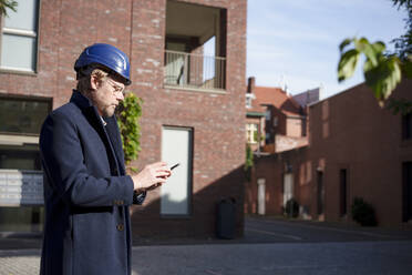 Architekt benutzt Smartphone vor einem Gebäude - KNSF10005