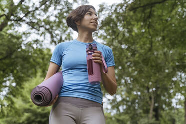 Frau mit Wasserflasche und Übungsmatte im Park stehend - OSF02342