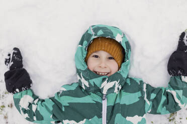 Junge im Grundschulalter trägt eine Jacke und liegt im Schnee - ONAF00694