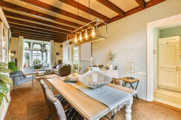 Illuminated pendant lights hanging over wooden table and chairs in dining room at modern house - ADSF49818