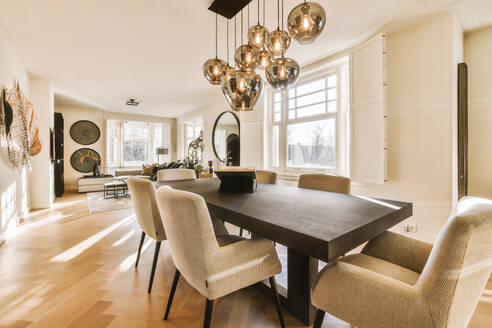 Pendant lights hanging over wooden dining table and white chairs in spacious dining room at modern light home - ADSF49820