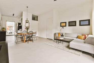 Comfortable couch with dining table and chairs arranged in spacious living room at modern white apartment - ADSF49830