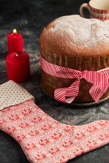 Panettone, the classic Italian treat, sits beautifully next to glowing red candles and a festive patterned stocking, capturing the essence of Christmas celebrations - ADSF49837