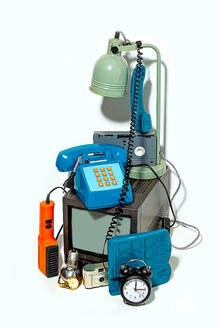 Eine kuratierte Sammlung alter technischer Geräte vor einem weißen Hintergrund, darunter ein alter Fernseher, ein Telefon mit Drehscheibe, ein Wecker, eine Schreibtischlampe und einige andere Retro-Geräte. - ADSF49842