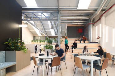 Busy coworking office in Madrid, Spain, showcasing professionals engaged in various activities the interior boasts an industrial design with plants, seating areas, and exposed ducts - ADSF49855
