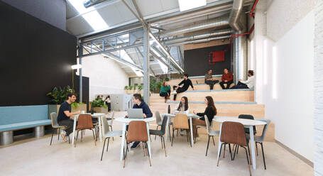 Busy coworking office in Madrid, Spain, showcasing professionals engaged in various activities the interior boasts an industrial design with plants, seating areas, and exposed ducts - ADSF49856