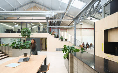 Spacious coworking office in Madrid, Spain, showcasing a blend of modern design with industrial elements professionals working and a foreground laptop on a wooden table - ADSF49858