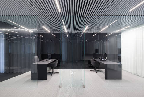An upscale office interior emphasizing bold patterns with stripe-designed ceilings, illuminating lights, and reflective glass dividers surrounding a modern desk and chair setup - ADSF49883
