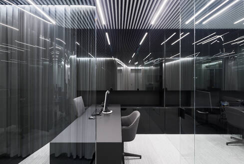 An office interior emphasizing bold patterns with stripe-designed ceilings, illuminating lights, and reflective glass dividers surrounding a modern desk and chair setup - ADSF49884