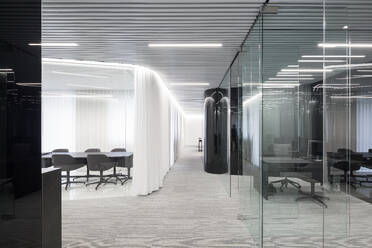 A modern office space featuring sleek design with horizontal lines on the ceiling, glass partitions, and a well-lit conference area with dark chairs - ADSF49885