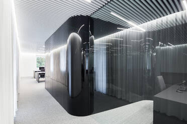 A modern office space showcasing an artistic design with translucent curved partitions, sleek furniture, and an intricately patterned ceiling illuminated by soft, diffused lighting. - ADSF49886