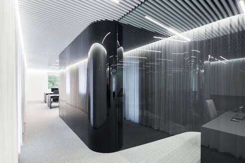 A modern office space showcasing an artistic design with translucent curved partitions, sleek furniture, and an intricately patterned ceiling illuminated by soft, diffused lighting. - ADSF49886