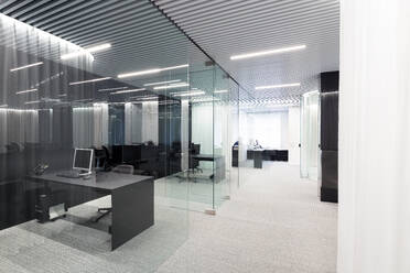 A modern office space featuring sleek design elements such as a dark desk, glass partitions, and overhead linear lighting - ADSF49888