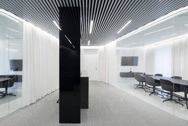 A modern office space featuring a sleek design with contrasting black and white elements. The ceiling showcases alternating black and white linear patterns, leading to the room's focal point, a black central column - ADSF49889