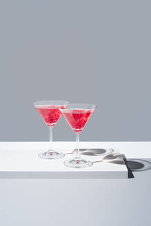 Glasses filled with red pomegranate cocktails against a muted gray backdrop, casting a soft shadows - ADSF49892