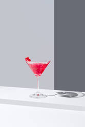 Glass filled with red pomegranate cocktails served with pomegranate seeds against a gray backdrop, casting a soft shadow - ADSF49893