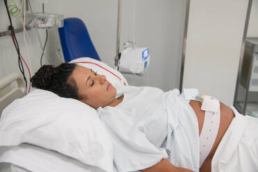 Close-up of a serene pregnant woman resting in a hospital bed, connected to medical devices, emphasizing the peace and trust in healthcare - ADSF49903