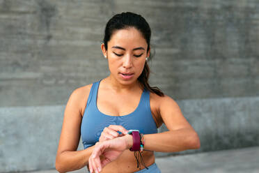 A Latin American woman checks her smartwatch during a workout session, monitoring her fitness goals. - ADSF49911