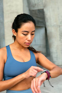 Eine lateinamerikanische Frau in Activewear konzentriert sich auf ihre Smartwatch, die vielleicht ihren Trainingsfortschritt oder ihre Herzfrequenz überwacht. - ADSF49912