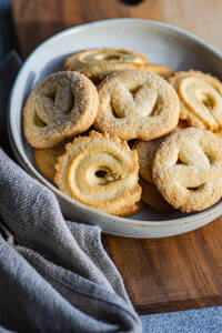 From above fresh homemade baked butter cookies placed in a bowl on a wooden cutting board beside a gray napkin, set against a minimalist concrete background - ADSF49922