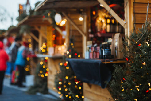 A cozy Christmas market stall adorned with warm lights and holiday decorations captures the festive spirit of the season as visitors browse nearby. - ADSF49940