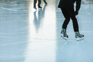 Close-up of ice skater's feet on a shiny outdoor rink, with others in the background. - ADSF49941