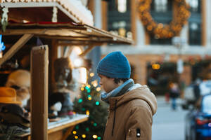 A man in a blue beanie and winter coat shops at an outdoor Christmas market stall adorned with festive decorations in Quebec, Canada - ADSF49942