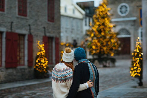 A romantic couple hugging in a charming street decorated with sparkling Christmas trees and vintage architecture in Quebec, Canada - ADSF49943