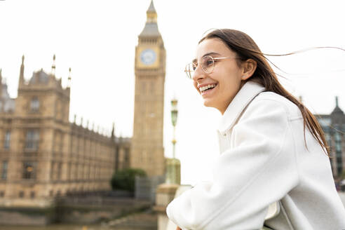 A joyful woman wearing stylish sunglasses smiles brightly while sightseeing, with the iconic Big Ben and the Houses of Parliament in the background. - ADSF49965