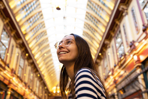 A cheerful young woman in striped attire admires the architecture of an iconic covered market in London. - ADSF49969