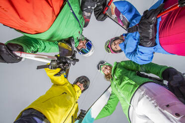 A dynamic low-angle shot captures a group of skiers forming a circle on a snowy landscape, dressed in vibrant ski apparel. - ADSF49974