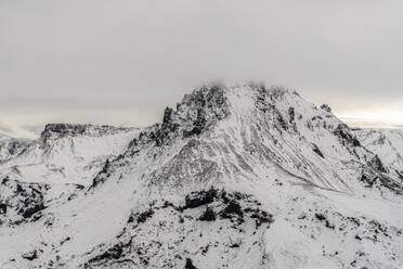 Aerial view of snow-covered mountain range with intricate patterns of rock and snow under a brooding sky - ADSF49976