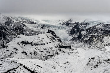 Aerial view of snow-covered mountain range with intricate patterns of rock and snow under a brooding sky - ADSF49977