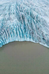 From above aerial drone view of glacier meeting the sea water with blue textured ice in Vatnajokull National Park located in Iceland in winter - ADSF49982