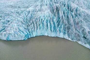 From above aerial drone view of glacier meeting the sea water with blue textured ice in Vatnajokull National Park located in Iceland in winter - ADSF49983