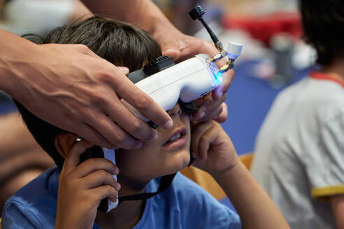 Young little amazed boy experiencing virtual reality with modified VR goggles at a drone exhibition while assisted by an adult cropped unrecognizable parent - ADSF49989