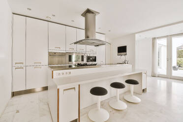 Interior of kitchen with stools placed by island and modern appliances with white cabinets at contemporary apartment - ADSF49996