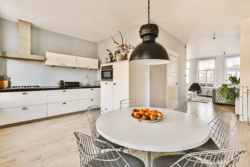 Pendant light hanging over round dining table and chairs in front of open plan kitchen at modern apartment - ADSF50008