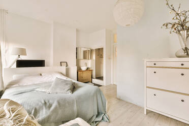 Comfortable bed with flower vase on dresser in spacious bedroom with white walls at contemporary apartment - ADSF50009