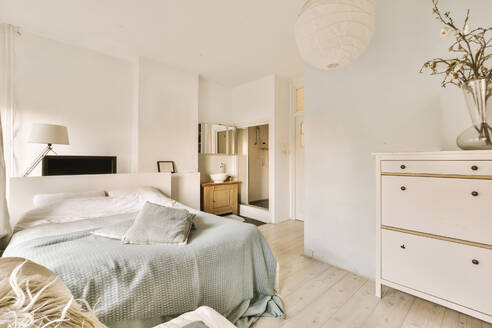 Comfortable bed with flower vase on dresser in spacious bedroom with white walls at contemporary apartment - ADSF50009
