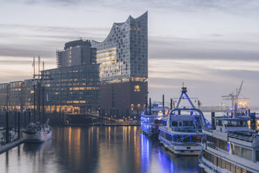 Germany, Hamburg, Boats moored in front of Elbphilharmonie at dusk - KEBF02801