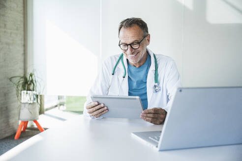 Zufriedener Arzt bei einem Videogespräch über einen Tablet-PC am Schreibtisch - UUF30615