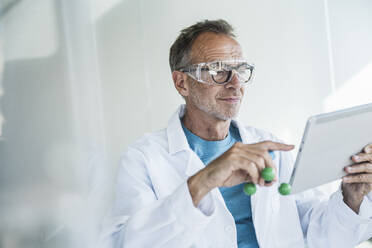 Lächelnder Mann im Laborkittel an einem Tablet-PC mit Molekularstruktur in der Nähe der Wand - UUF30619