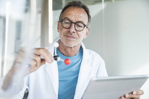 Senior man in lab coat holding tablet PC and examining molecular structure - UUF30626