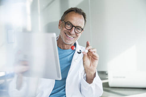 Glücklicher älterer Mann im Laborkittel mit Tablet-PC und Molekularstruktur - UUF30628