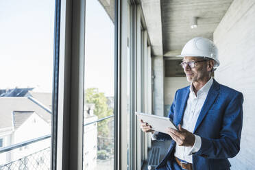 Smiling engineer holding tablet PC and standing near window - UUF30650