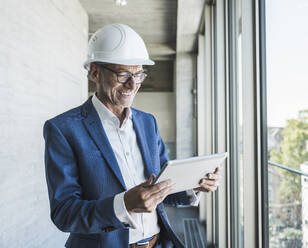 Happy senior engineer using tablet PC near window in corridor - UUF30651